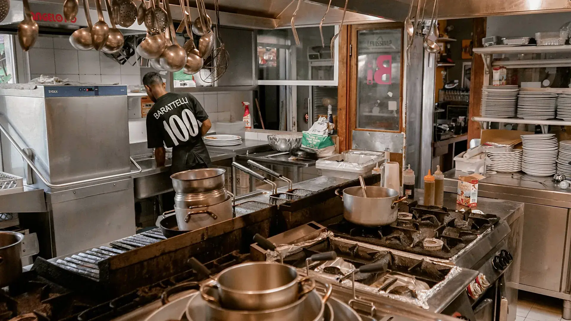 Interno della cucina con cuoco di spalle mentre cucinaSa